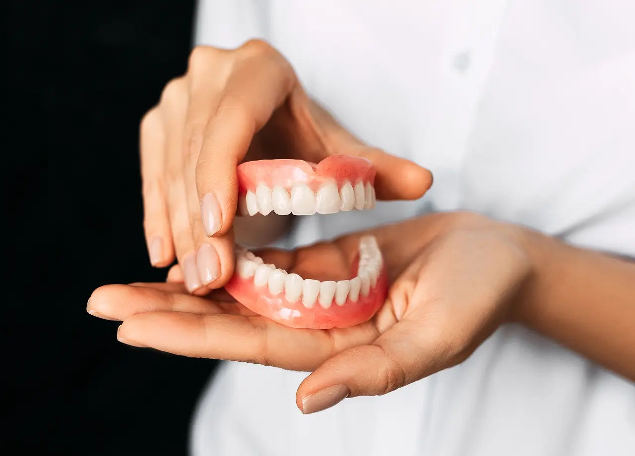 Hands holding upper and lower dentures.